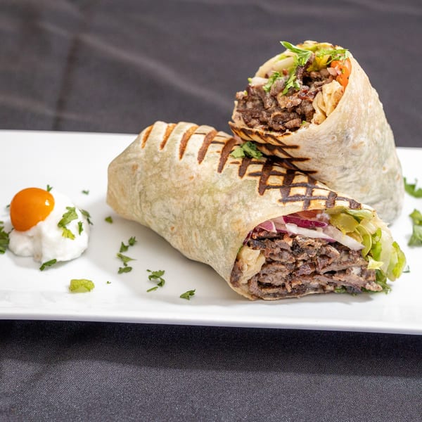 Two grilled beef shawarma wraps with lettuce, onions, and sauce on a white plate.