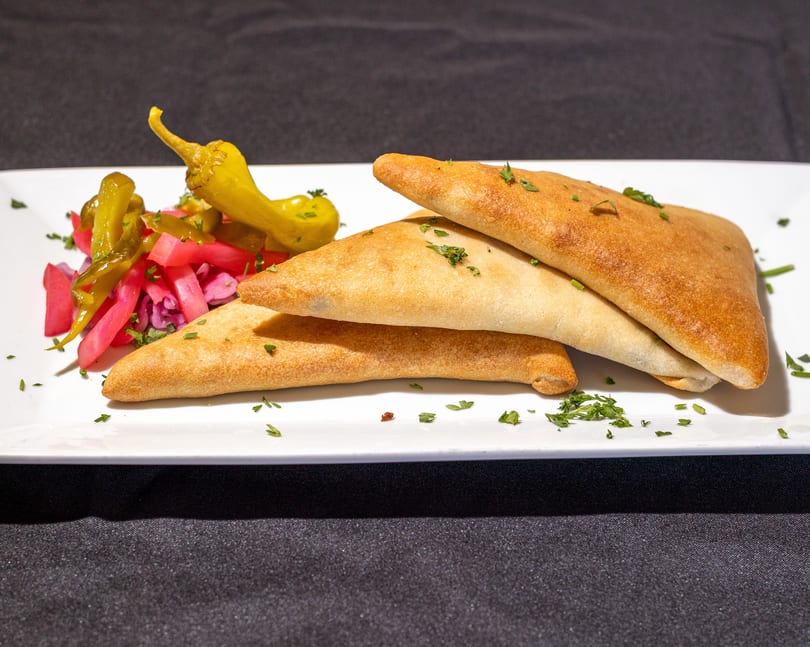 Three golden-brown pastries with pickled vegetables and peppers on a white rectangular plate.