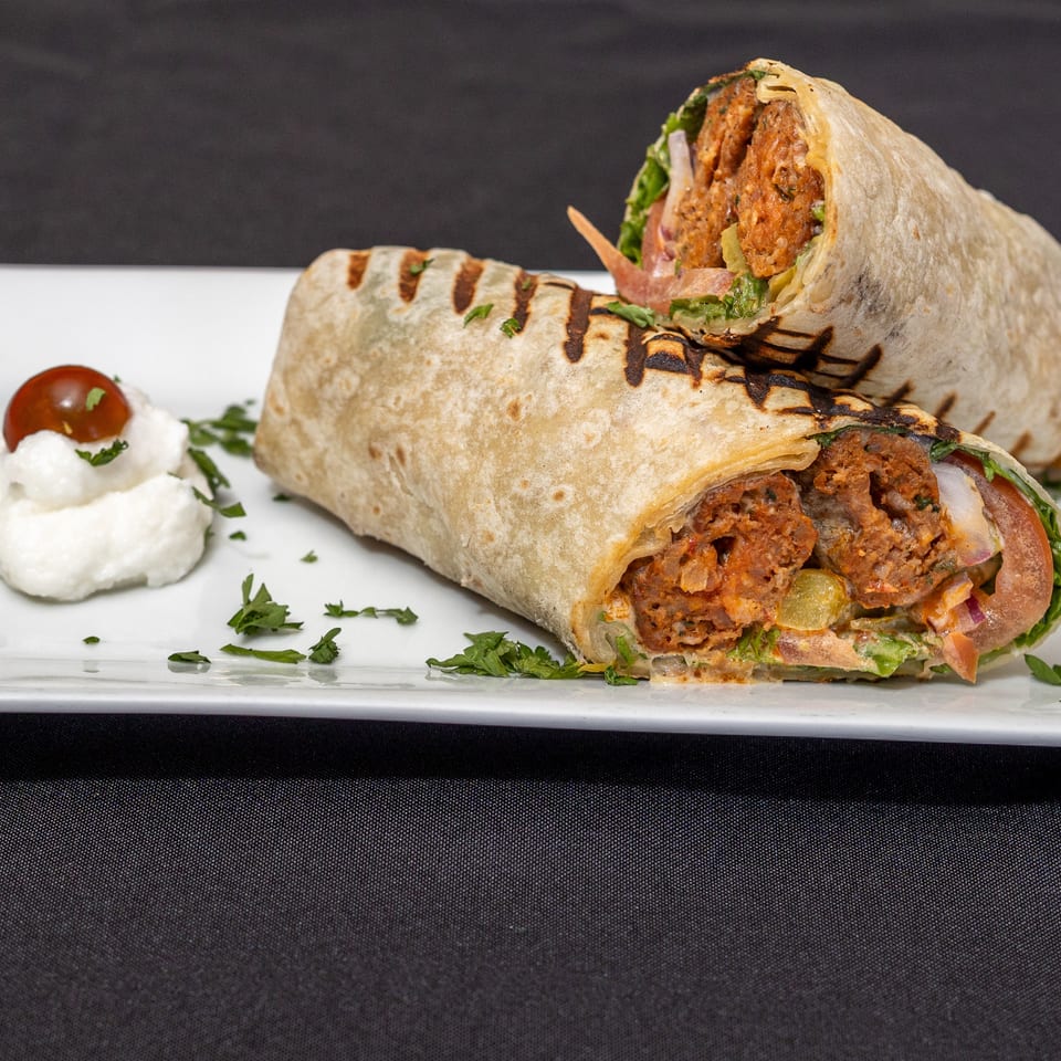 Two grilled wraps filled with meat, lettuce, and sauce, served with a dollop of white cream and a cherry tomato.