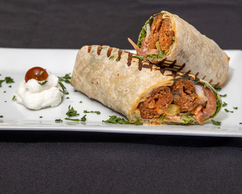 Two grilled wraps filled with meat, lettuce, and sauce, served with a dollop of white cream and a cherry tomato.