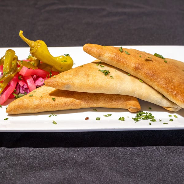 Three golden-brown savory pastries, garnished with parsley, served with pickled vegetables and peppers on a white plate.