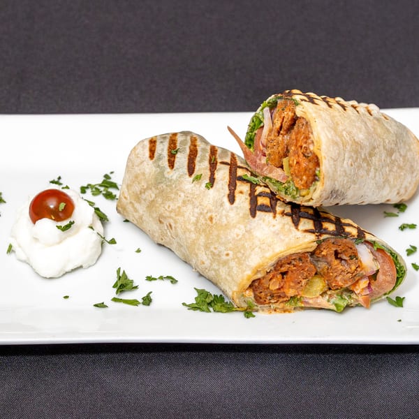Two grilled wraps filled with meat, lettuce, and tomato, served with a dollop of cream.