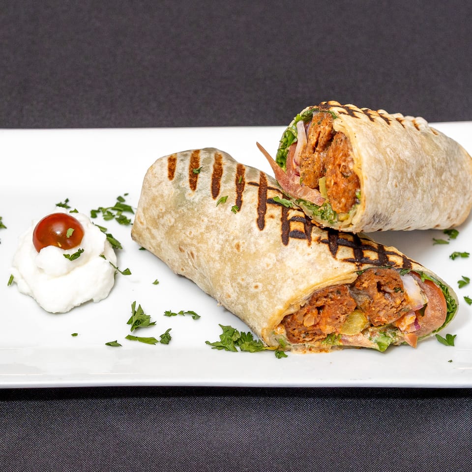 Two grilled wraps filled with meat, lettuce, and tomato, served with a dollop of cream.