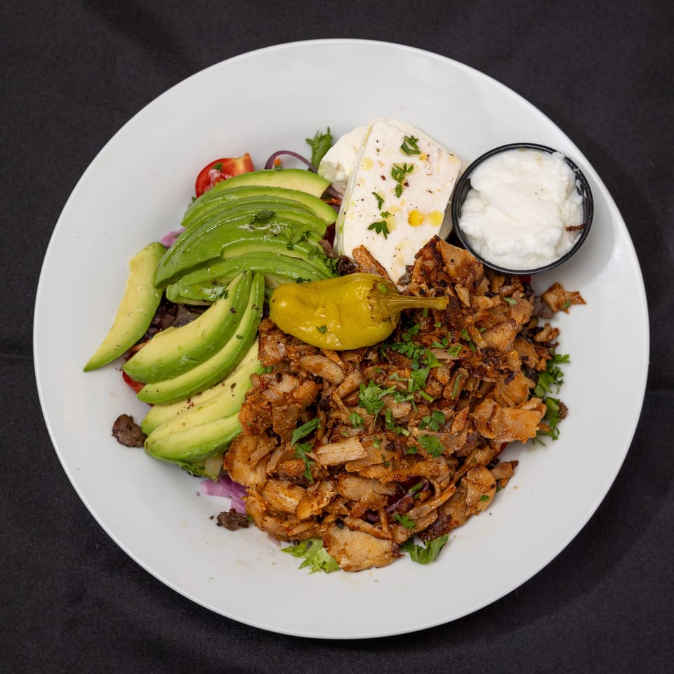 Gyro plate with sliced avocado, feta cheese, tzatziki, and a yellow pepper on a white plate.