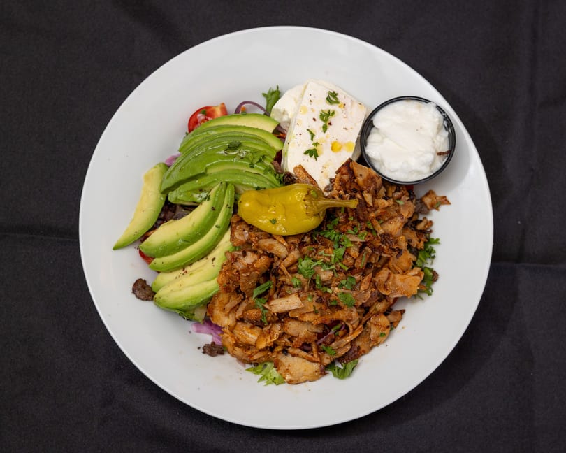 Gyro plate with sliced avocado, feta cheese, tzatziki, and a yellow pepper on a white plate.