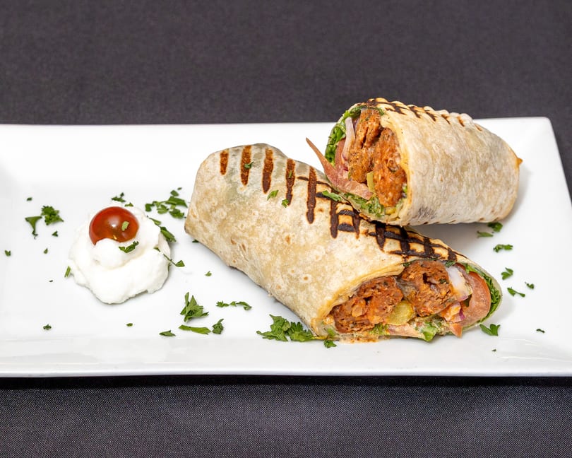 Two grilled wraps filled with meat, lettuce, and tomato, served with a dollop of cream and cherry tomato.