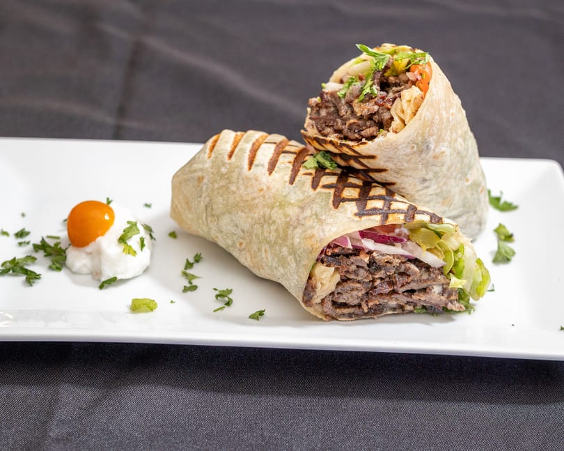 Two grilled beef shawarma wraps with lettuce, onions, and sauce on a white plate.
