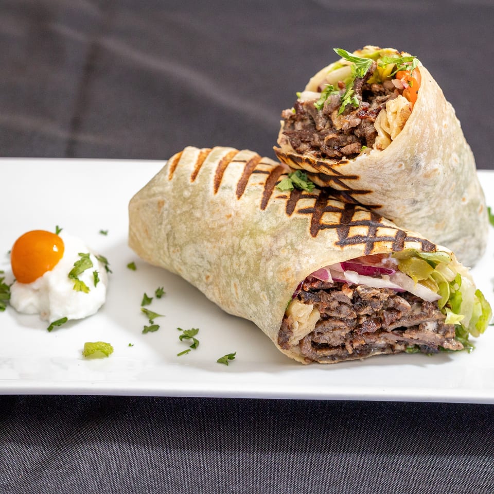 Two grilled shawarma wraps filled with meat, lettuce, and onions, served with a side of sauce.