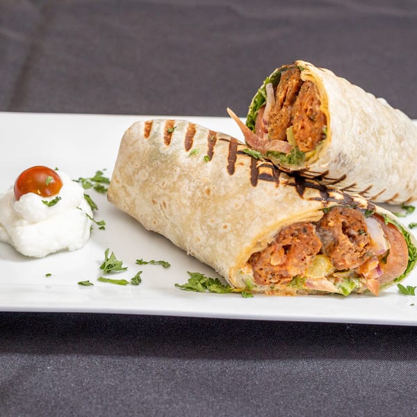 Two grilled wraps filled with meat and vegetables, served with a dollop of white sauce and a cherry tomato.