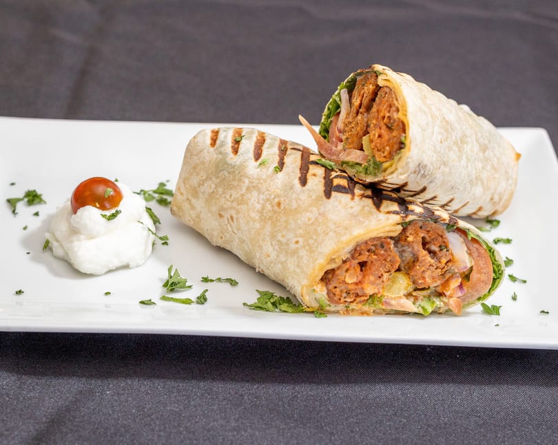 Two grilled wraps filled with meat and vegetables, served with a dollop of white sauce and a cherry tomato.
