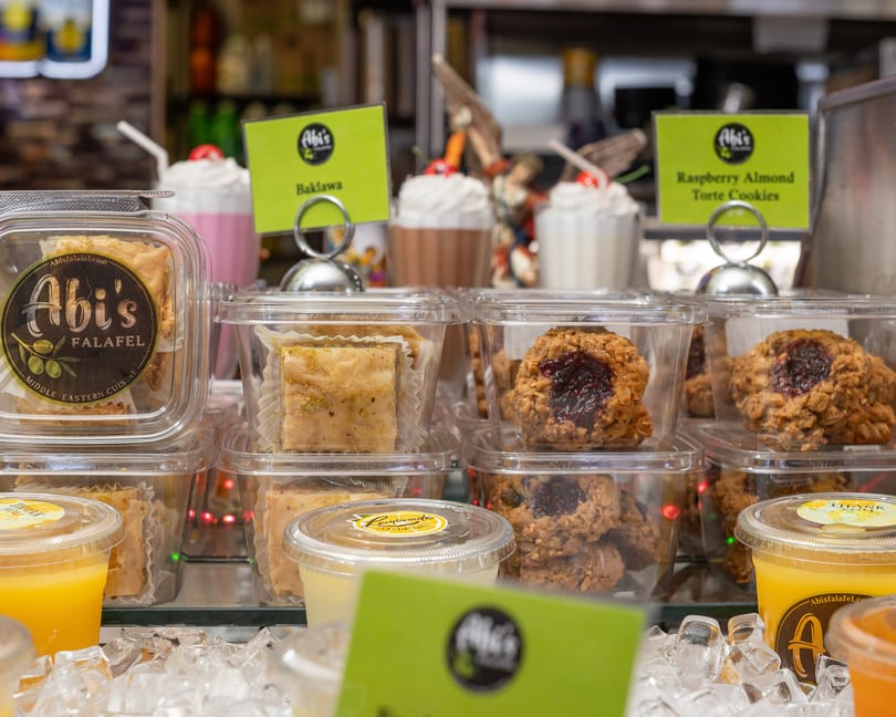 Abi's Falafel baklava, raspberry almond torte cookies, and drinks displayed in a refrigerated case.